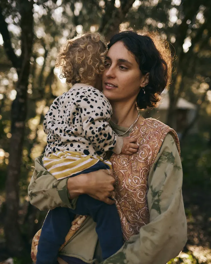 ema carrying her youngest child on her hip among the trees