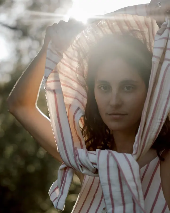 ema holding a striped cloth above her head, backlit by the sun